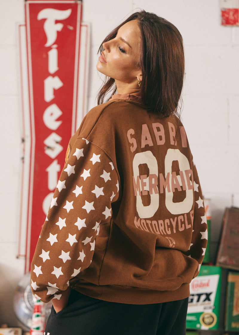 Person wearing a brown sweatshirt with star patterns and visible branding in an indoor setting.