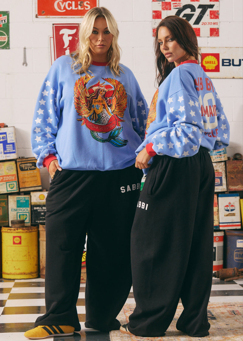 Two people wearing matching blue sweatshirts with graphic designs in a garage setting.