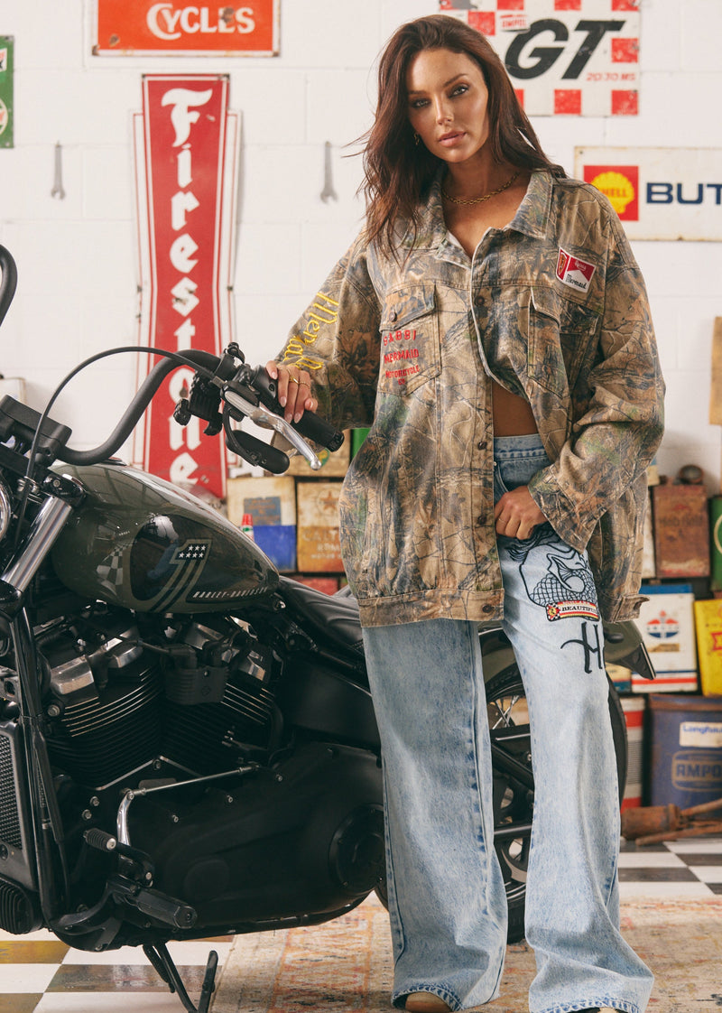 Woman standing next to a motorcycle in a garage with vintage signs in the background