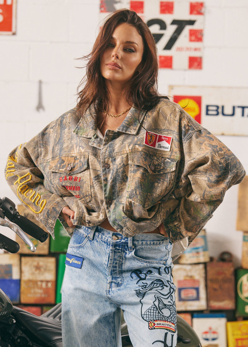 Woman wearing a camouflage jacket with patches in a garage setting