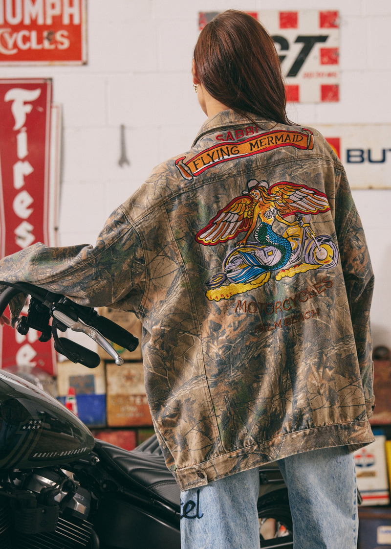 Person wearing a jacket with a 'Flying Mermaid' patch in a garage setting