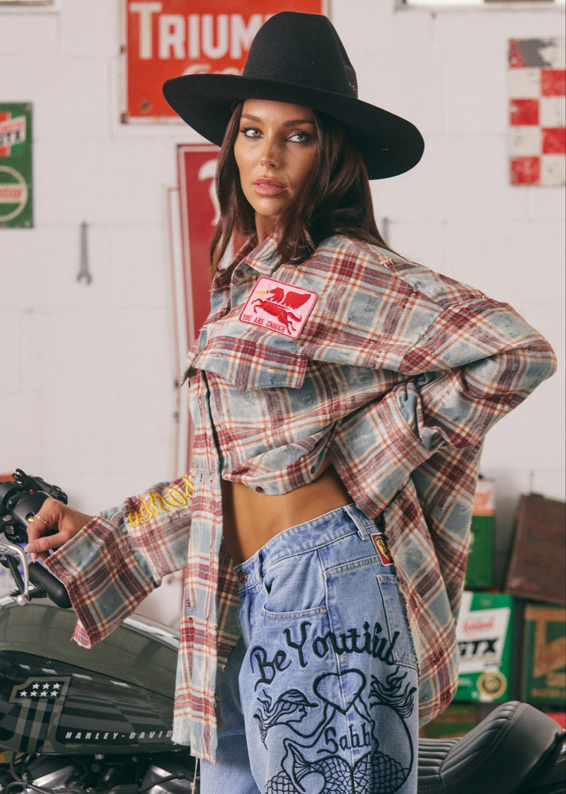Woman wearing a plaid shirt and jeans with a motorcycle in the background