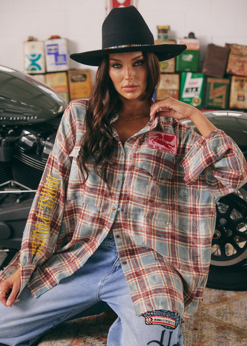 Woman wearing a plaid shirt with patches in a garage setting