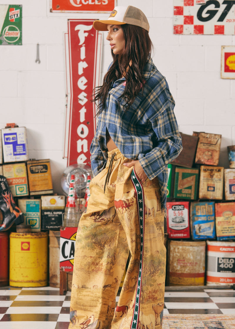 Person wearing a plaid shirt and beige pants in a garage setting with vintage signs and equipment.