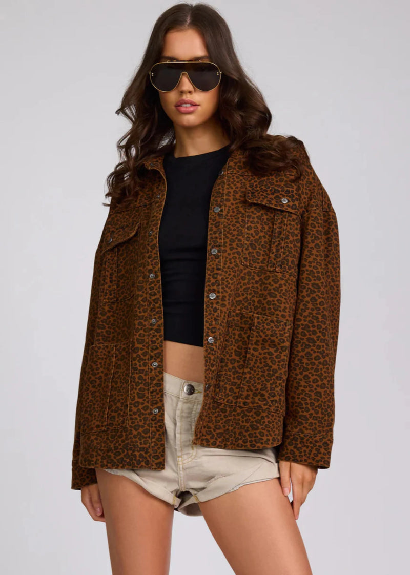 Woman wearing a brown leopard print jacket over a black top and beige shorts on a gray background