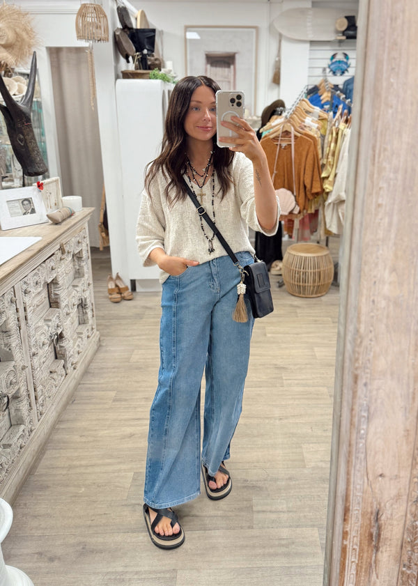 Woman taking a mirror selfie in a store wearing a beige sweater and blue jeans.